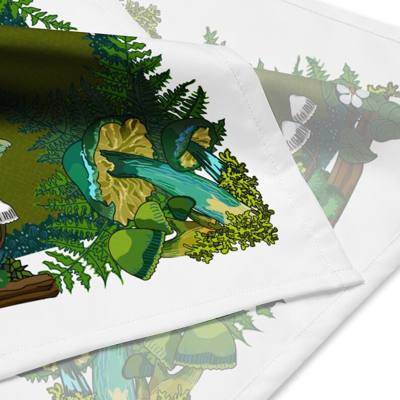 This is a close-up image of the bandana scarf folded over. It shows the pattern that includes green mushrooms, ferns, twigs, and mosses. The color palette is greens, turquoise blue, white, and a bit of brown.