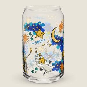 May include: A clear glass can-shaped drinking glass with a celestial design. The design includes gold stars, a crescent moon, blue clouds, and a hand holding stars. Other elements include arrows, matches, and starbursts.