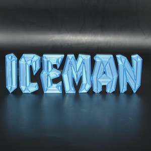 May include: The word "ICEMAN" is displayed in a light blue, geometric font. The letters appear to be 3D printed and have a crystalline appearance, with facets that catch the light. The background is a dark, reflective surface.