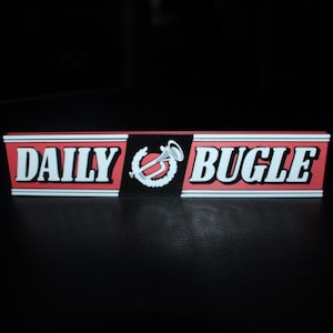 May include: A rectangular sign with the words "DAILY BUGLE" in white, bold letters on a red background. A black section in the middle features a white emblem. The sign is likely a prop or collectible.