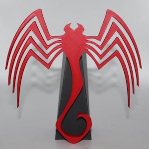 May include: A red and black decorative emblem, featuring a stylized wing-like design with multiple lines and a central, elongated shape. The emblem is mounted on a dark gray, triangular base. The overall design is symmetrical and bold.
