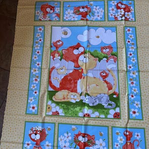 May include: A fabric panel featuring a repeating pattern of cartoon cats, flowers, and bees. The cats are primarily orange and yellow, set against a light blue background. The panel has a yellow dotted background and floral borders.