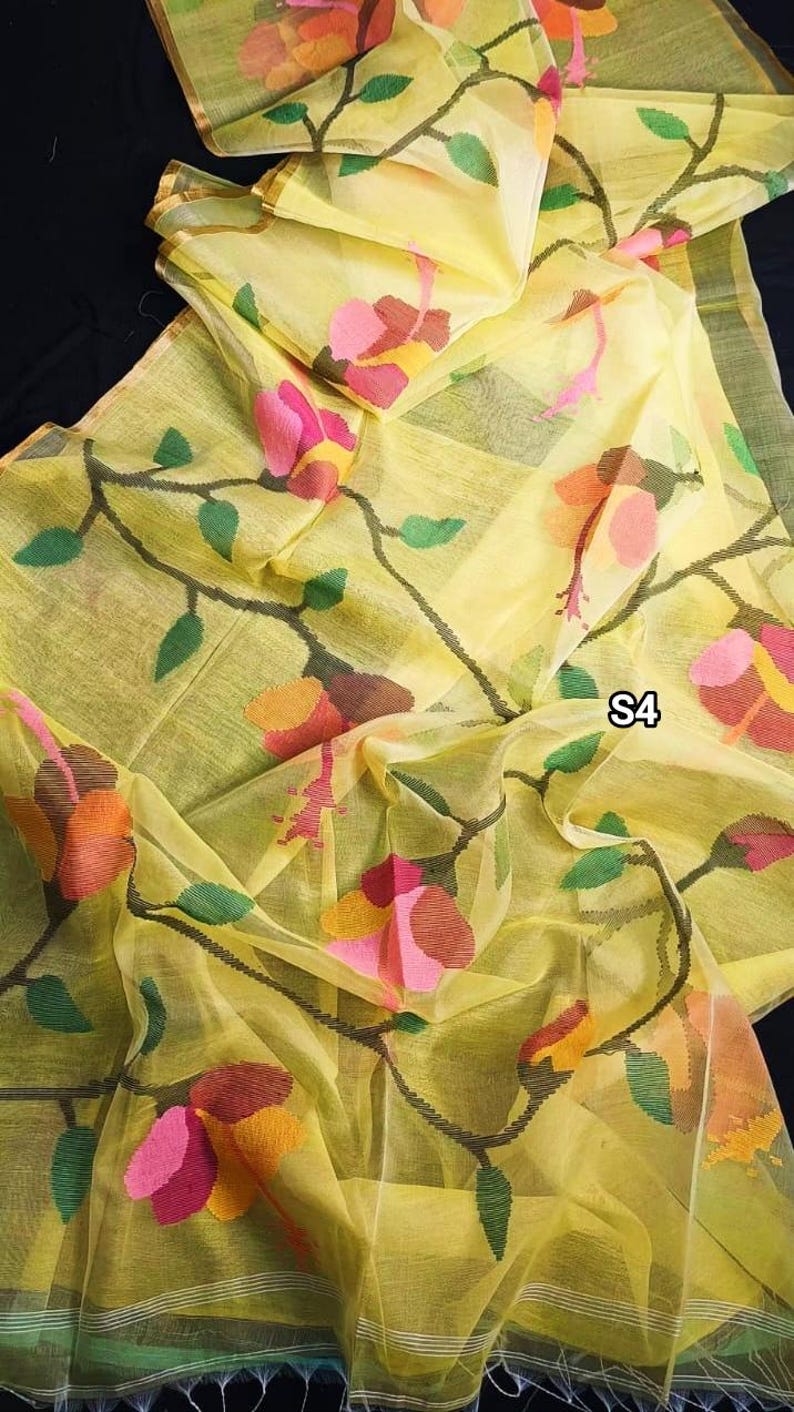 May include: A yellow sheer saree with a floral pattern in shades of pink, orange, and green. The saree has a delicate, almost translucent quality and features a subtle sheen. The fabric is lightweight and drapes beautifully.