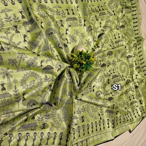 May include: A light green textile with a black illustrated village scene. The fabric has a shiny appearance and features detailed drawings of people, houses, and trees. The edge of the textile is trimmed with a black border. The text "S1" is visible.