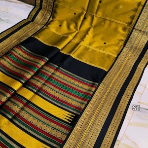 May include: A mustard yellow and black saree featuring a wide border with intricate gold zari patterns, accented by horizontal stripes in red and green. The main fabric displays small black dots, and the text S1 is visible in the corner.