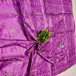 May include: A vibrant purple silk saree with intricate gold-colored patterns. The saree features detailed designs along the borders and across the fabric, with a small green plant in the center. The tag "S8" is visible.