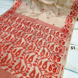 Op de afbeelding: Een beige textiel met een rood bloemmotief en rand. Het ontwerp bevat herhalende blad- en geometrische vormen. Het textiel heeft een gestreepte rand. De tekst "S1" is zichtbaar.