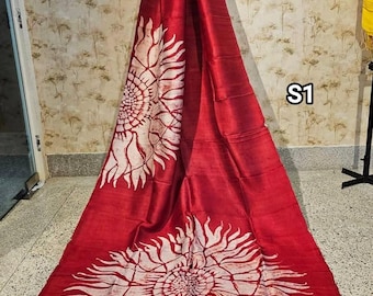 May include: A red silk saree with white sunflower designs. The saree has a cream colored border. The saree is hanging on a wall with the text "S1" visible.