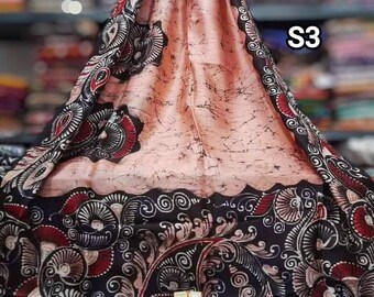 May include: A pink and black silk saree with a floral pattern. The saree is draped over a table and has a tag that says "S3".