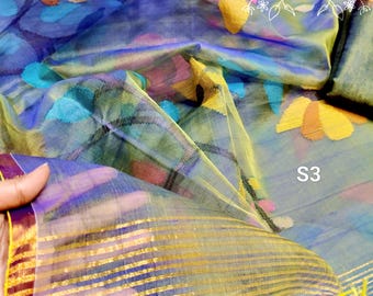 May include: A sheer blue fabric with a floral pattern in yellow, pink, and orange. The fabric features a gold striped border and the text SHYETA with a decorative frame and the label S3. The material has a translucent, lightweight texture.