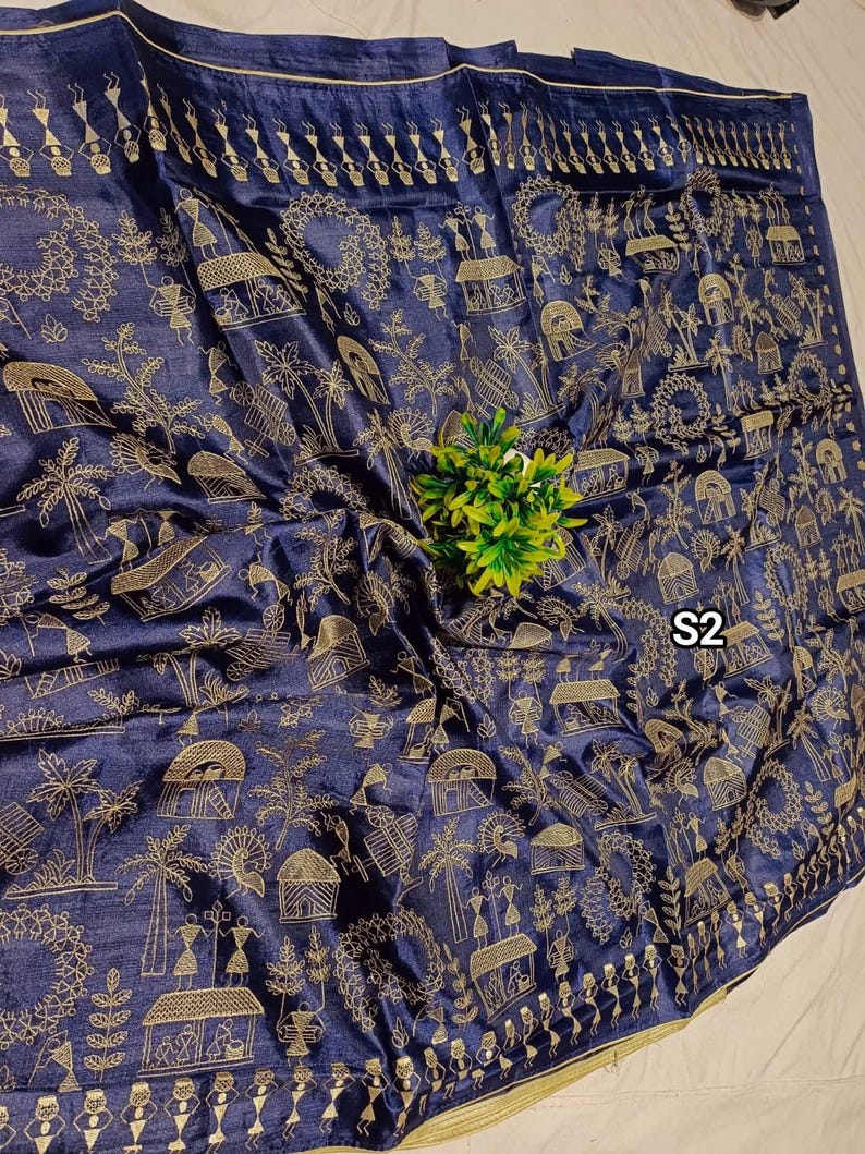 May include: A navy blue textile with a gold-colored pattern featuring stylized figures, trees, and huts. The fabric has a subtle sheen and a decorative border. The text "S2" is visible on the fabric.