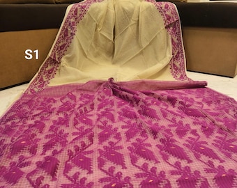 May include: A cream-colored saree with a purple floral pattern and border. The saree is draped over a brown sofa. The border features an intricate design. The text "S1" is visible in the image.