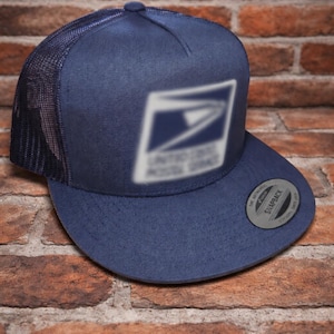 May include: Navy blue trucker hat with a mesh back and a flat brim. The front panel features a blurred white graphic of the United States Postal Service logo. The hat has a snapback closure and a curved brim.