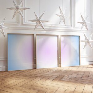Pode incluir: Três cartazes com moldura dourada com um fundo degradê de azul, roxo e rosa. Os cartazes estão pendurados em uma parede branca com molduras decorativas brancas.