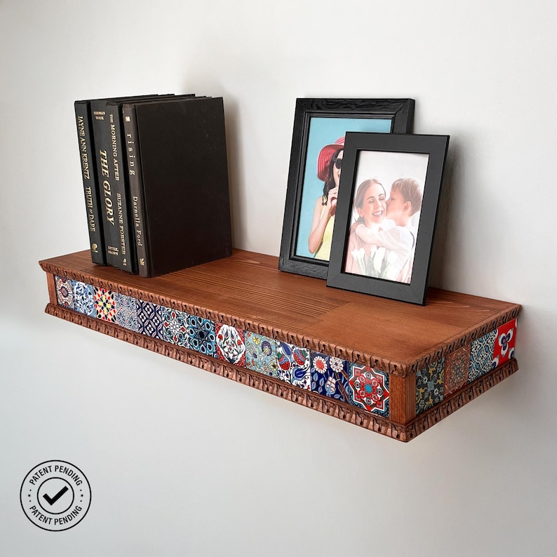 May include: A wooden floating shelf featuring a front edge decorated with a row of colorful, patterned ceramic tiles. Three black books and two black picture frames containing photographs are positioned on the top surface of the shelf.