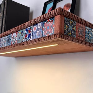 May include: A wall-mounted wooden shelf featuring a row of decorative tiles with intricate floral and geometric patterns in red, blue, and white. The shelf has a carved wooden border and an integrated LED light strip along the underside.