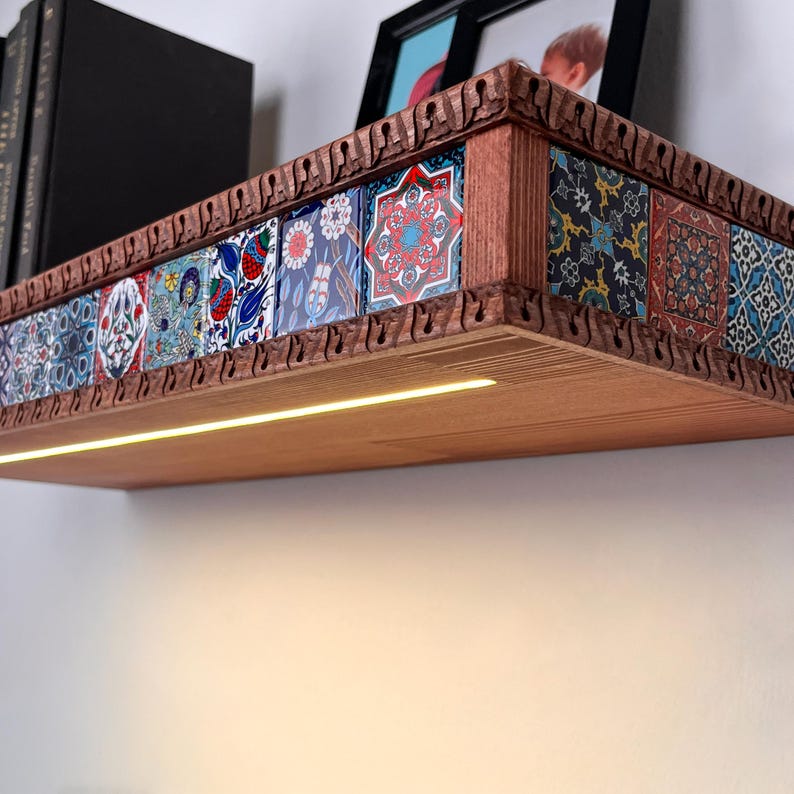 May include: A wall-mounted wooden shelf featuring a row of decorative tiles with intricate floral and geometric patterns in red, blue, and white. The shelf has a carved wooden border and an integrated LED light strip along the underside.