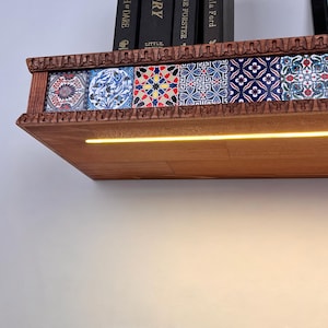 May include: A wooden wall shelf featuring a row of six decorative tiles with intricate blue, red, and white geometric and floral patterns. The shelf has a carved edge and an integrated horizontal LED light strip that emits a warm yellow glow.