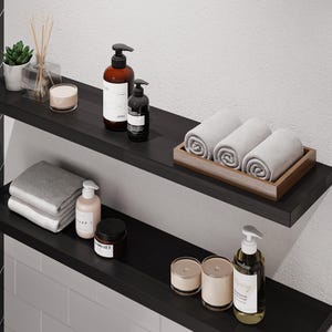May include: Two black shelves with various bathroom products, including towels, candles, and bottles of lotion. The shelves are mounted on a white wall.