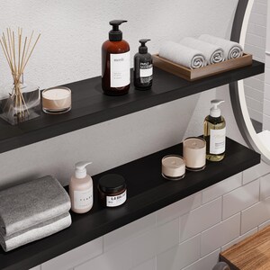 May include: Two black floating shelves with various bathroom items, including two bottles of hand soap, a diffuser, candles, and towels. The shelves are mounted on a white tiled wall.