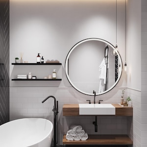 May include: A modern bathroom with white subway tile walls, a white freestanding bathtub, a round mirror with a black frame, a wooden vanity with a white sink, and black fixtures.
