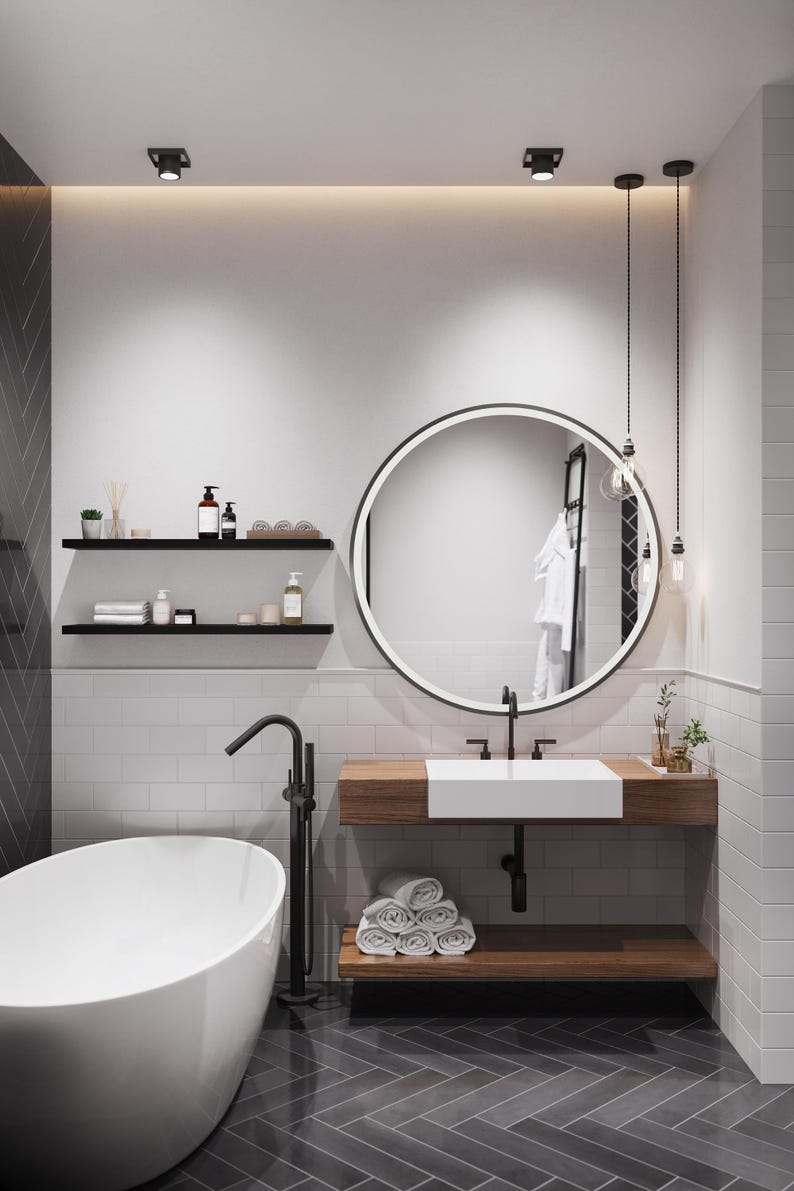 May include: A modern bathroom with white subway tile walls, a white freestanding bathtub, a round mirror with a black frame, a wooden vanity with a white sink, and black fixtures.