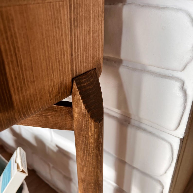 May include: Close-up of a wooden chair with a light brown finish. The chair has a curved seat and back, with a single leg angled outward. The wood grain is visible, and the chair appears to be well-crafted.