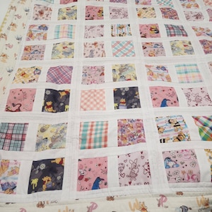 May include: A patchwork quilt featuring a grid of square fabric panels with various Winnie the Pooh character prints, including Piglet, Eeyore, and Tigger, separated by white sashing. The border displays a repeating pattern of Pooh and Eeyore.
