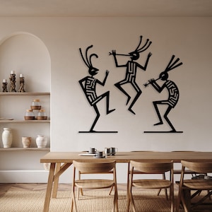 Puede incluir: Arte mural de metal negro que representa tres figuras estilizadas en una pose de baile. Las figuras tienen cuerpos alargados y tocan instrumentos musicales. La obra de arte está montada en una pared de color neutro sobre una mesa de comedor de madera.