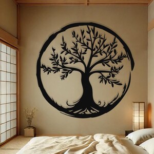 Peut inclure: Un autocollant mural en forme d'arbre de vie noir et blanc dans un cercle sur un mur beige. L'autocollant est au-dessus d'un lit futon avec une couette beige et deux oreillers blancs. La pi&egrave;ce a un plafond en bois et une porte coulissante avec un cadre en bois.