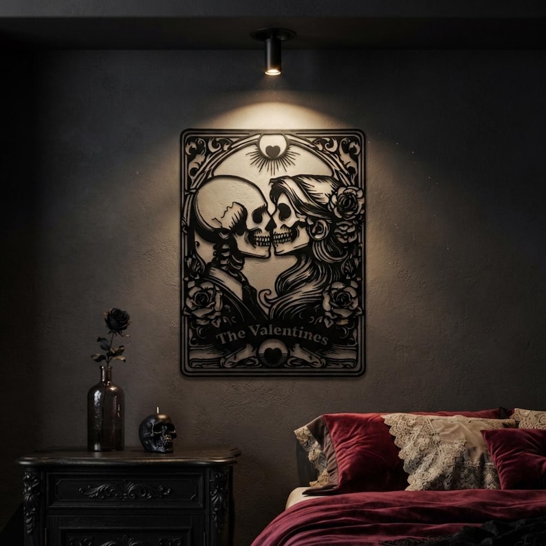 May include: A black metal wall art piece featuring a stylized illustration of two skulls facing each other, surrounded by floral motifs and a sun symbol. The text "The Valentines" is printed at the bottom of the rectangular frame design.