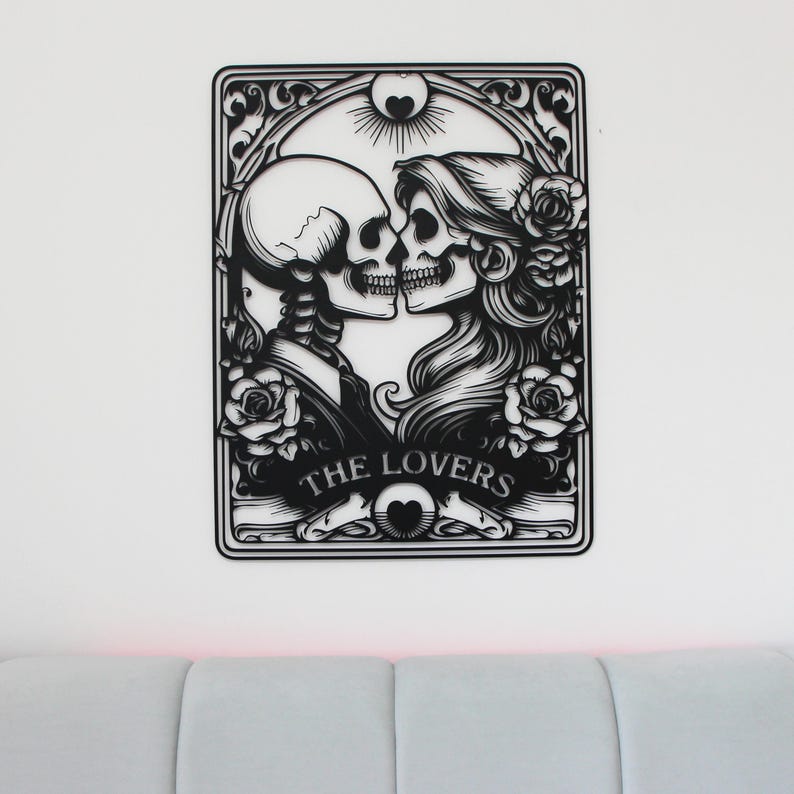 May include: A black metal wall art piece featuring a cutout design of two skeletons facing each other in a romantic pose. The artwork includes floral details, a sun motif at the top, and the text THE LOVERS inscribed at the bottom center.