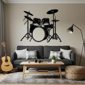 Puede incluir: Decoración mural de arte de batería de metal negro. El juego de batería incluye un bombo grande, cajas y platillos. El arte está montado en una pared beige sobre un sofá gris. Una guitarra y una lámpara también están en la habitación.