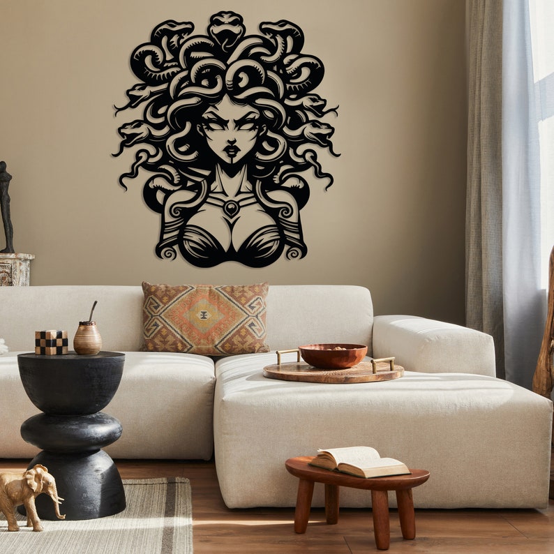 May include: Black and white wall art featuring a stylized illustration of Medusa, a Greek mythological figure with snakes for hair. The art is mounted on a beige wall above a white couch.