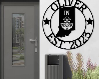 Może przedstawiać: Czarny metalowy znak z tekstem "Oliver Est. 2023" i obrysem stanu Indiana z oznaczeniem "IN" wewnątrz. Znak jest zawieszony na białej ścianie.