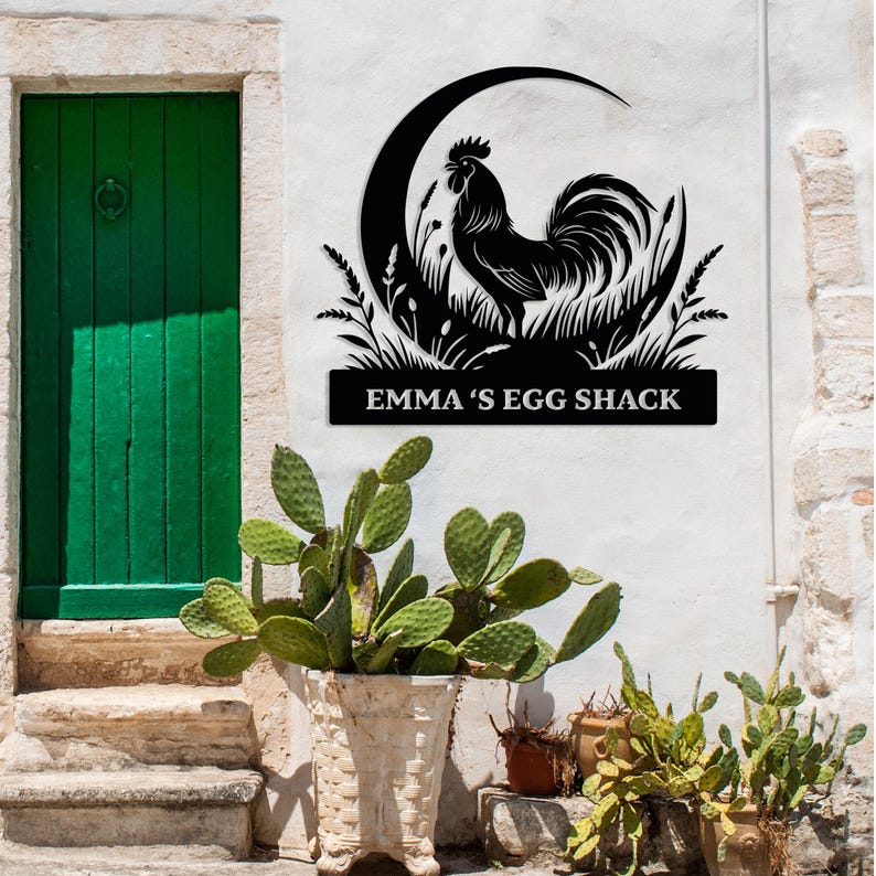 May include: Black metal rooster sign with the text "EMMA'S EGG SHACK" displayed on a white wall. The sign features a rooster silhouette within a crescent moon and grass design. A green door and potted plants are in the background.