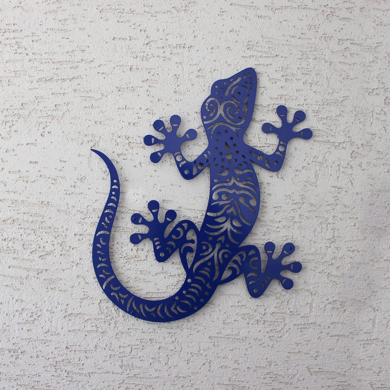 May include: A blue metal gecko wall decor with intricate patterns cut out of the metal. The gecko is in a climbing pose with its tail curled.
