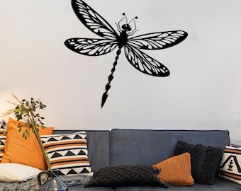 May include: Black silhouette of a dragonfly with intricate wing details, mounted on a white wall above a gray couch with throw pillows.