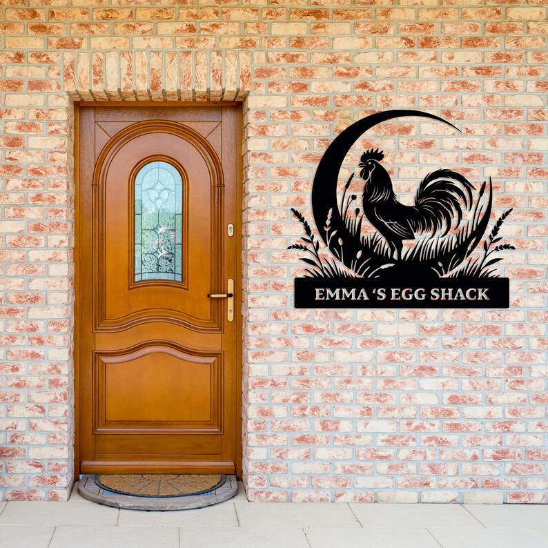 May include: Black metal sign featuring a rooster silhouette within a crescent moon and grass design. The sign reads "EMMA'S EGG SHACK" in white lettering. The sign is mounted on a brick wall next to a wooden door.