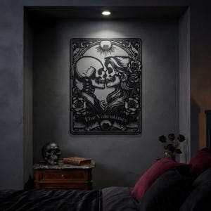 May include: A black metal wall art piece featuring a rectangular frame with a central illustration of two skulls facing each other. The design includes roses, a sunburst motif, and the text The Valentines printed in a banner at the bottom.