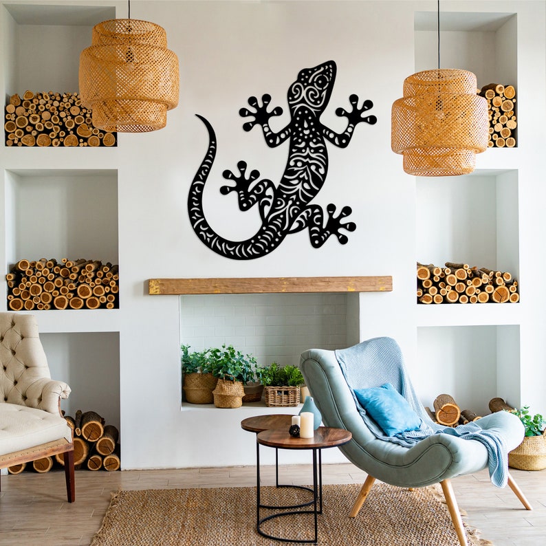 May include: Black metal wall art featuring a stylized gecko with intricate details. The gecko is mounted on a white wall in a living room setting with a fireplace, furniture, and decorative elements.