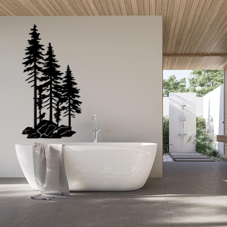 May include: A white bathtub with a gray towel draped over the side, set against a white wall with a black silhouette of three pine trees on a rocky landscape.