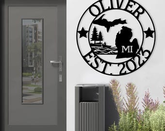 May include: Black metal sign with the state of Michigan, two pine trees, a boat with a person fishing, and the text "Oliver Est 2023 MI".