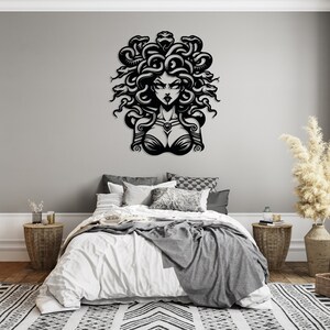 May include: Black and white wall art featuring a stylized illustration of Medusa, a Greek mythological figure with snakes for hair. The art is displayed above a bed with white bedding and gray throw blankets.
