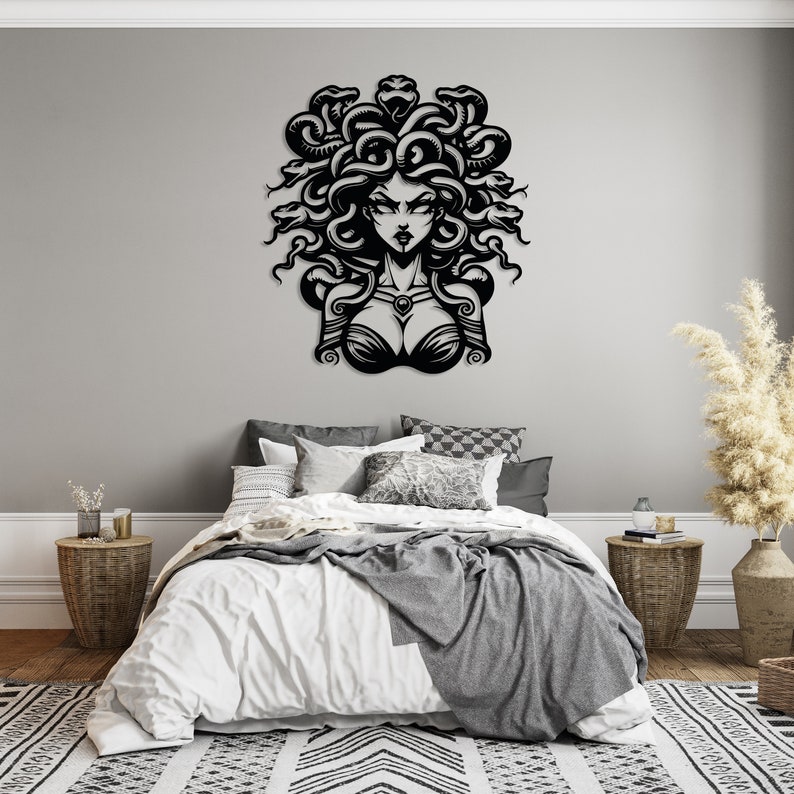 May include: Black and white wall art featuring a stylized illustration of Medusa, a Greek mythological figure with snakes for hair. The art is displayed above a bed with white bedding and gray throw blankets.