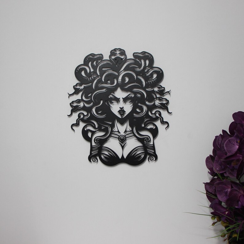 May include: Black and white silhouette of Medusa, a mythical Greek figure with snakes for hair, looking directly at the viewer. The image is a cutout design, possibly made of metal.