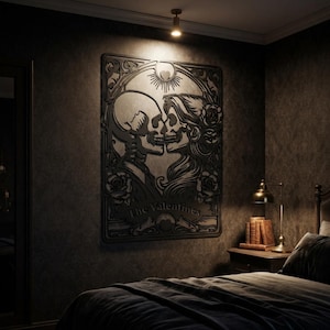 May include: A black wall art piece featuring a laser-cut design of two skeletons facing each other in a romantic pose, surrounded by floral motifs and a sunburst element. The text "The Valentines" is engraved at the bottom of the rectangular frame.