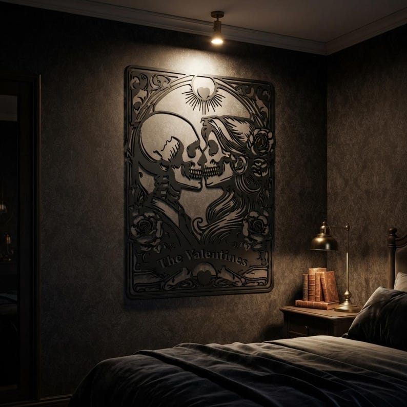 May include: A black wall art piece featuring a laser-cut design of two skeletons facing each other in a romantic pose, surrounded by floral motifs and a sunburst element. The text "The Valentines" is engraved at the bottom of the rectangular frame.