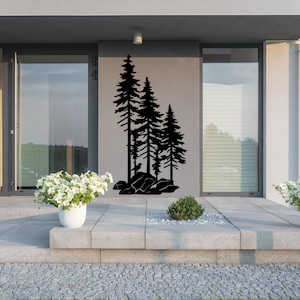 May include: Black silhouette of three pine trees on a gray wall. The trees are in a row, with the tallest tree in the center. The trees are set against a backdrop of a modern home with a patio.