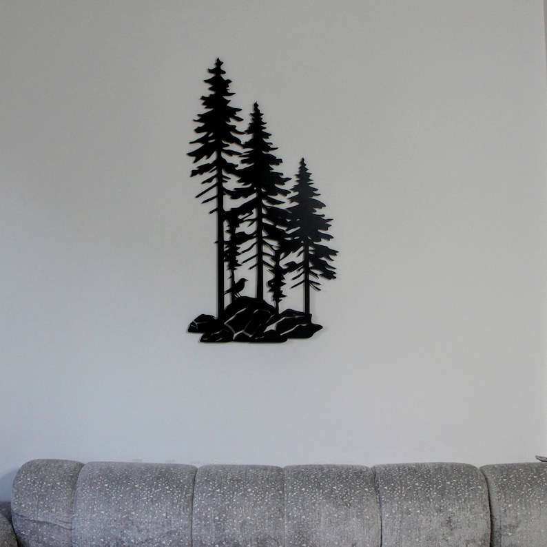 May include: Black metal wall art featuring a silhouette of three pine trees with a bird perched on a rock. The trees are arranged in a staggered formation, creating a visually appealing design.